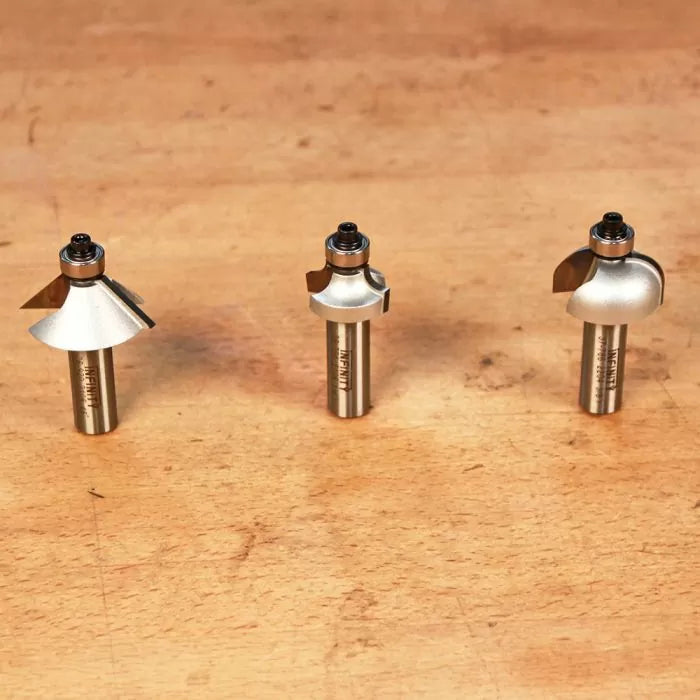 Three metal router bits with bearings on a wooden surface, woodworking tool set