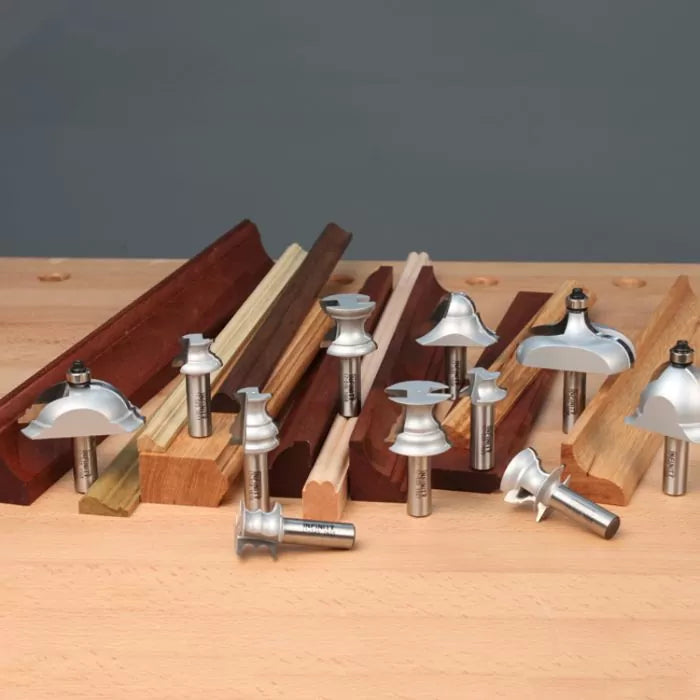 Assorted router bits for woodworking displayed on a workbench with moulded wood samples.