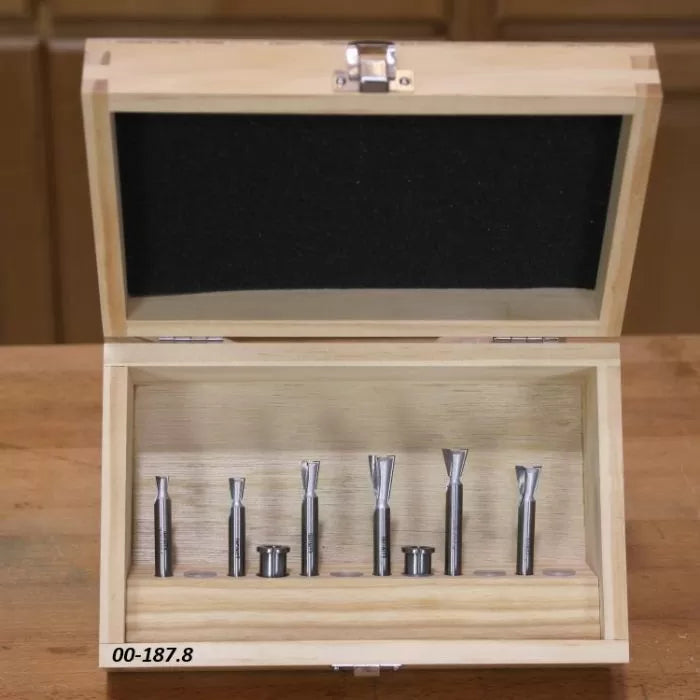 Woodworking router bit set in wooden case on workbench, seven metal bits displayed.
