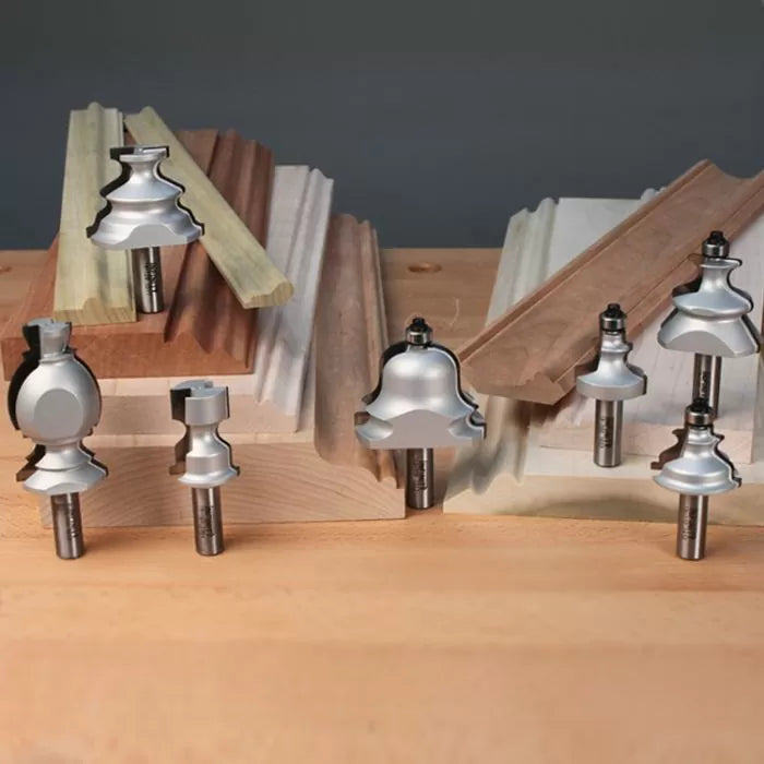 Assorted woodworking router bits displayed with decorative wood moulding samples on a workbench