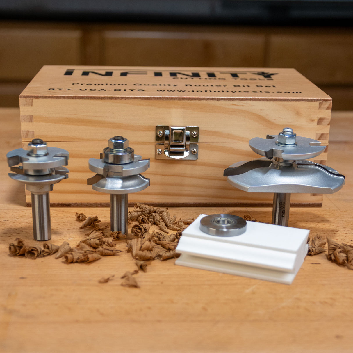 Woodworking router bit set with wooden storage box on a workbench, surrounded by wood shavings.