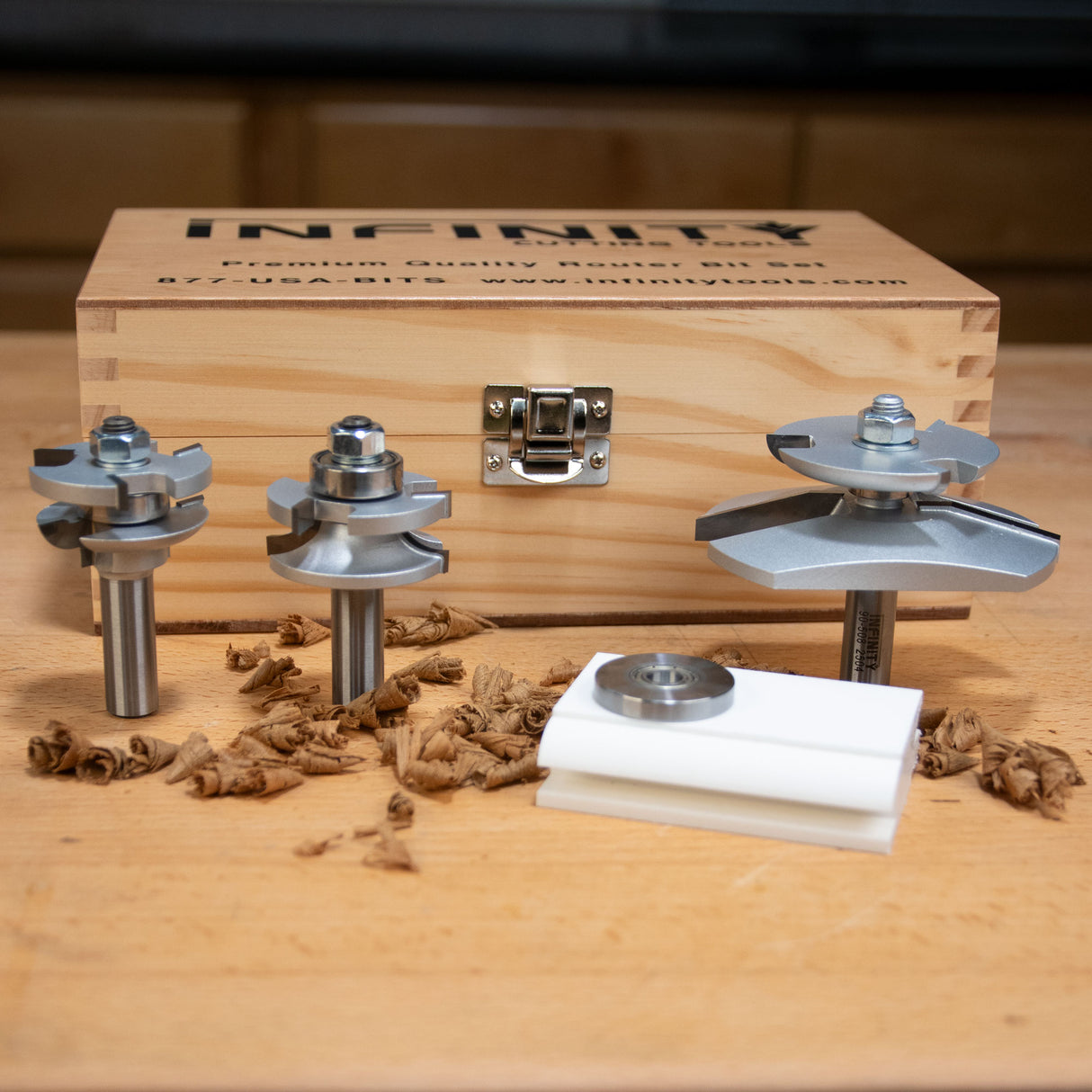 Woodworking router bit set with three steel router bits, wooden storage case, and accessories on a workbench.
