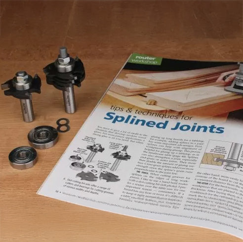 Router bits set with bearings and washers next to splined joints woodworking magazine on wood surface.