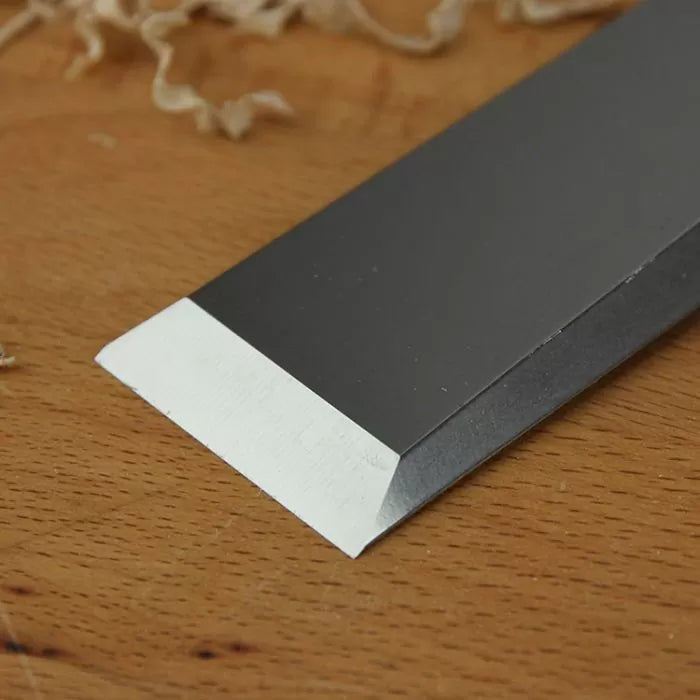Sharp woodworking chisel blade on wooden surface with wood shavings in background
