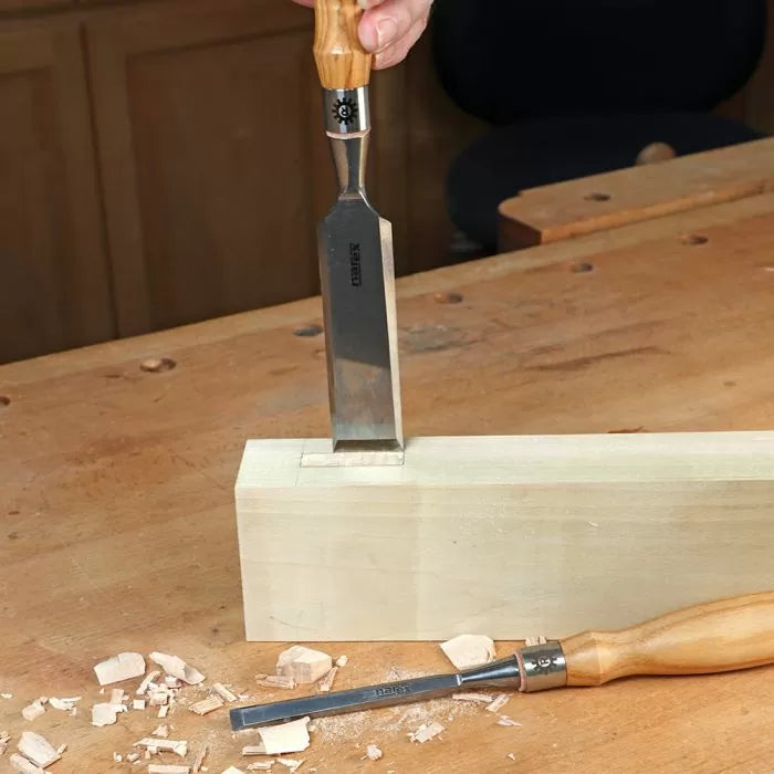 Woodworker chiseling mortise joint in hardwood block with woodworking chisel on bench