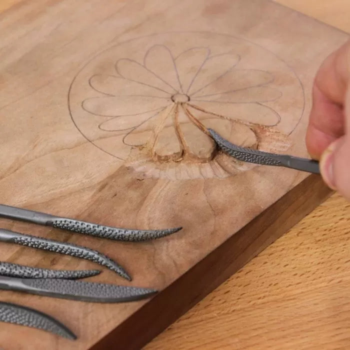 Hand carving wood flower design with curved wood rasps on a workbench