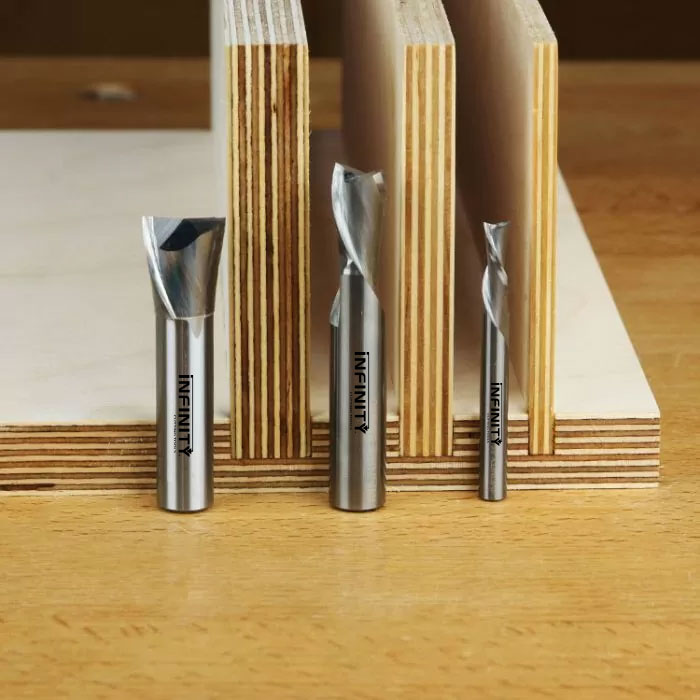 Carbide spiral router bits displayed upright in front of stacked plywood sheets on a workbench