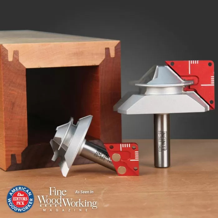 Lock miter router bits with red setup blocks on wood surface, next to a precisely joined wooden box.