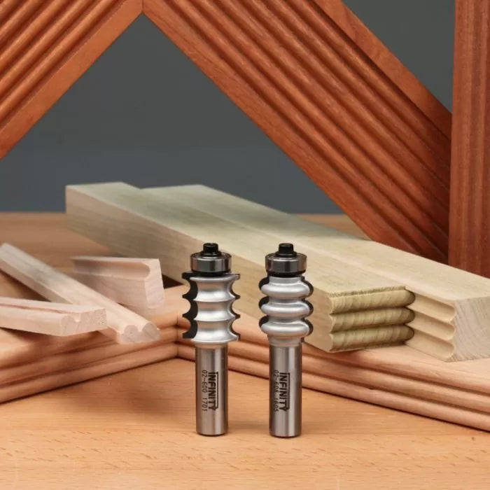 Two woodworking router bits with fluted profiles, displayed on a workbench with decorative moulding and wood trim pieces