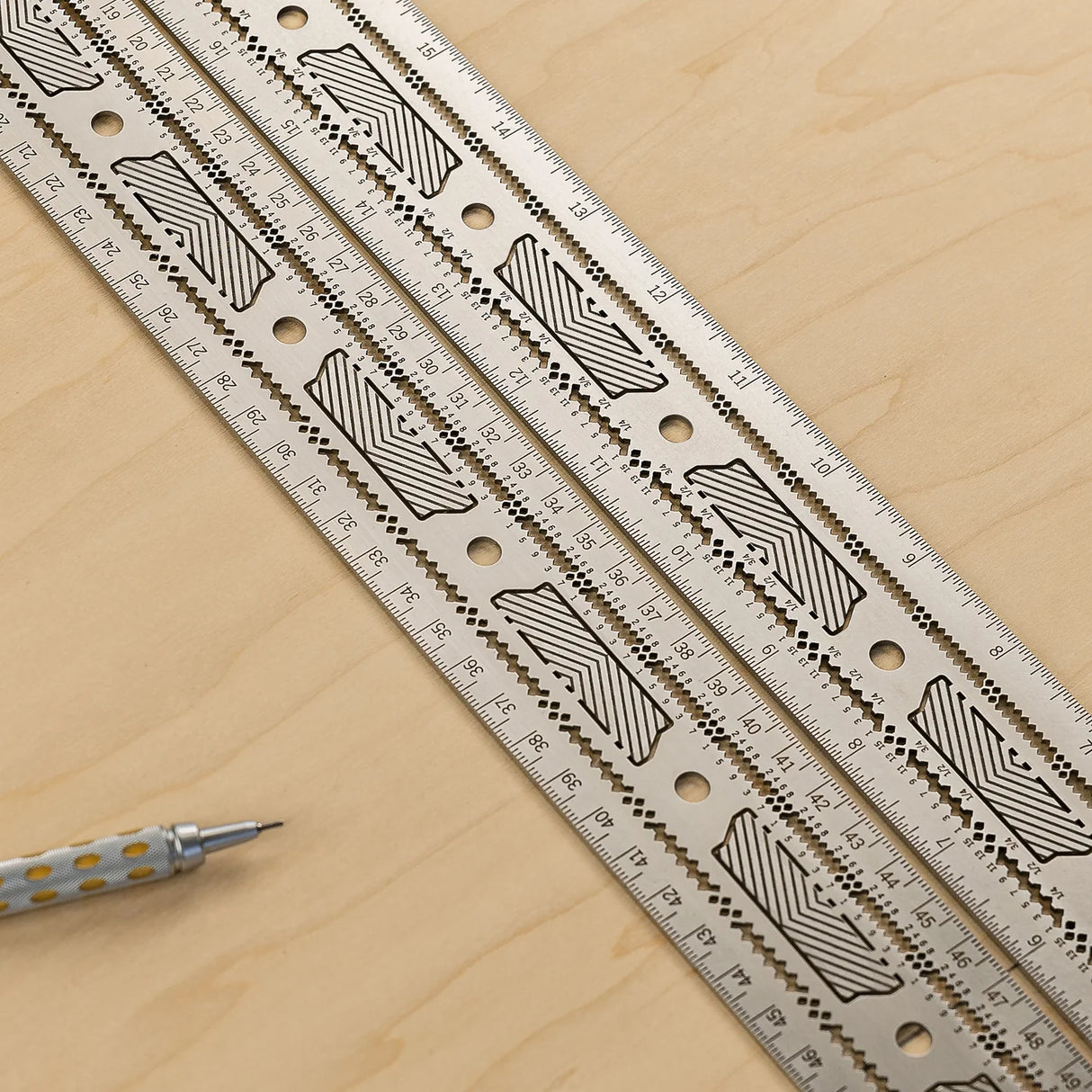 Stainless steel woodworking rulers with etched markings on a wood surface, mechanical pencil nearby.