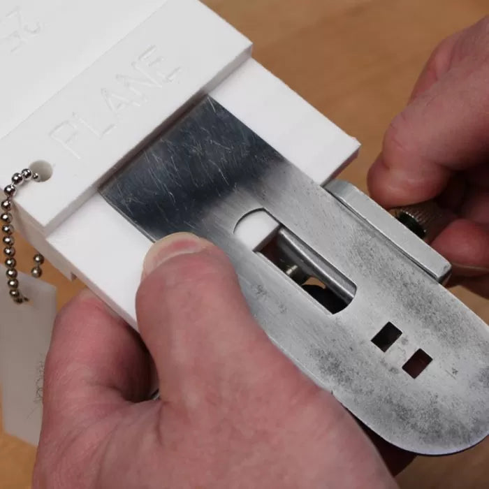 Hands using a jig to align and sharpen a woodworking plane blade on a workbench.