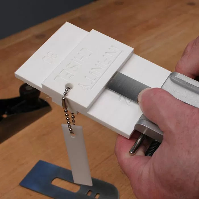 Woodworking chisel sharpening jig in use on workbench with hand tool accessories visible.