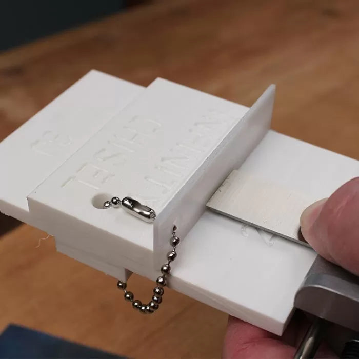 Woodworking chisel sharpening jig holding a chisel blade on a workbench