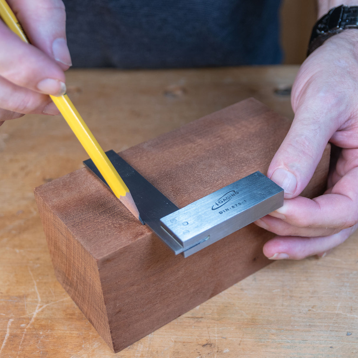 Woodworker using a precision square to mark a line on a wooden block