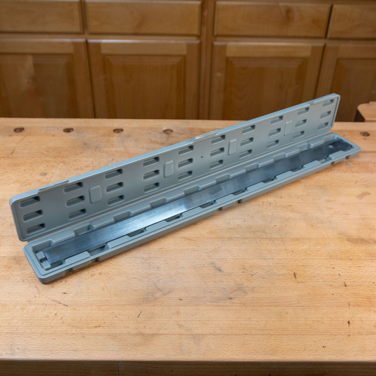 Woodworking planer blade in a gray storage case on a workshop bench