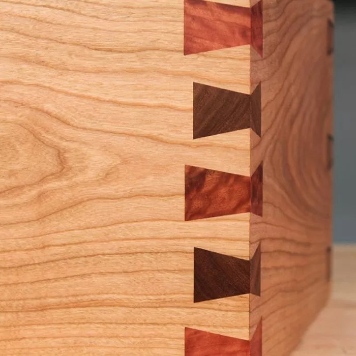 Close-up of a wooden box corner featuring precise dovetail joinery with contrasting wood inserts