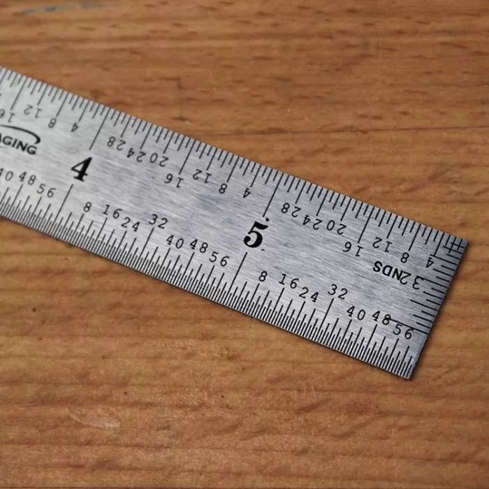 Stainless steel woodworking ruler with inch and metric markings on wooden surface