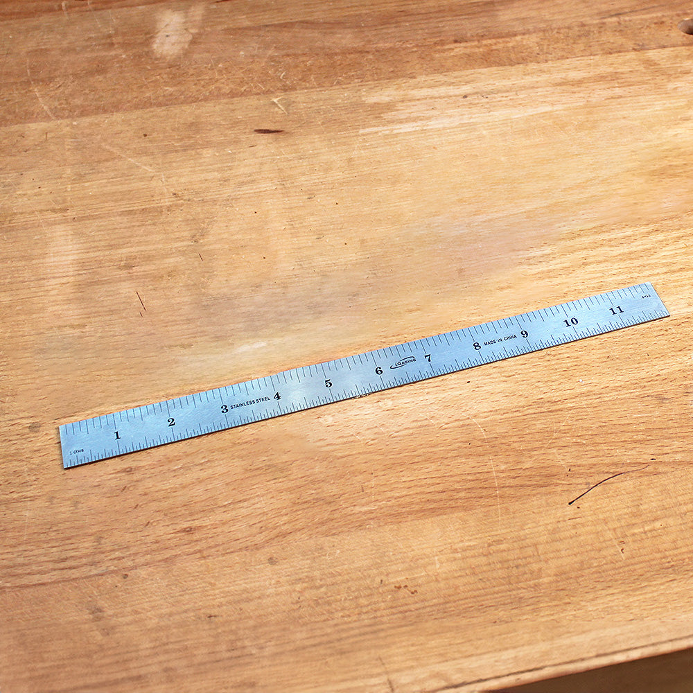 Stainless steel ruler with inch markings on a wooden workbench for woodworking measurement.