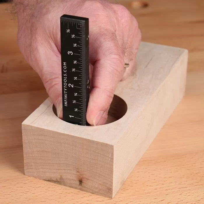 Measuring hole depth in wood block with a black precision ruler on a woodworking bench