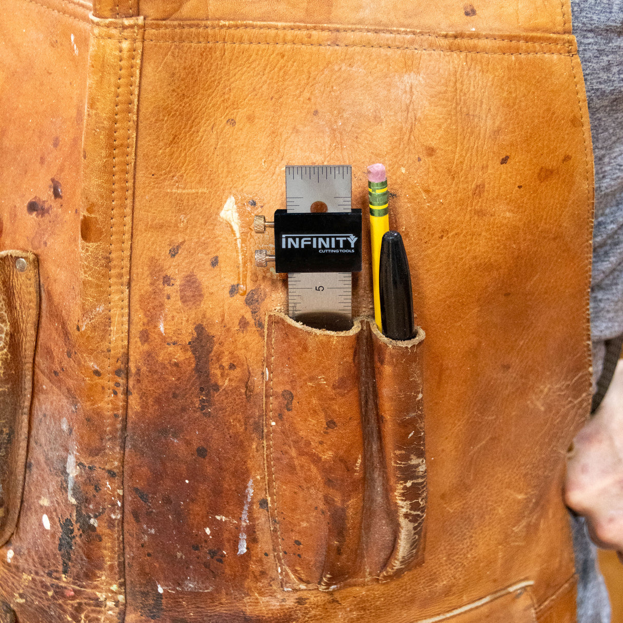 Vintage leather apron with a pocket holding a ruler and pencil, branded 'Infinity'.