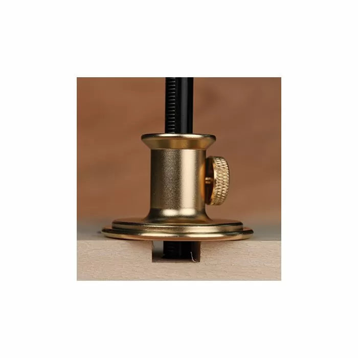 Brass woodworking marking gauge set on an edge of wood, close-up tool detail.
