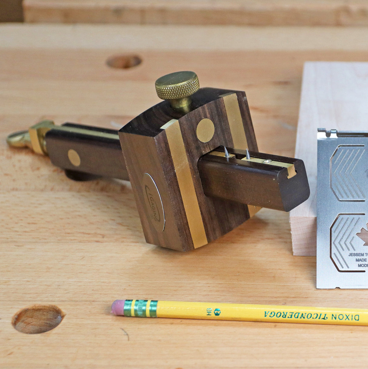 Wood marking gauge with brass accents on a workbench, next to a pencil and precision tool.