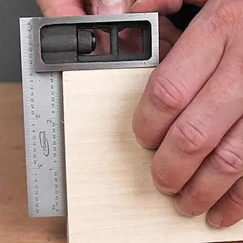 Hand using combination square to measure and mark wood for precise woodworking