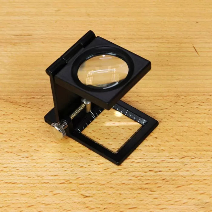 Folding linen tester magnifier tool with ruler on a wooden workbench