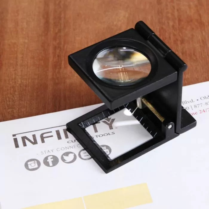 Folding magnifier tool with black frame on wooden table, ideal for woodworking precision.