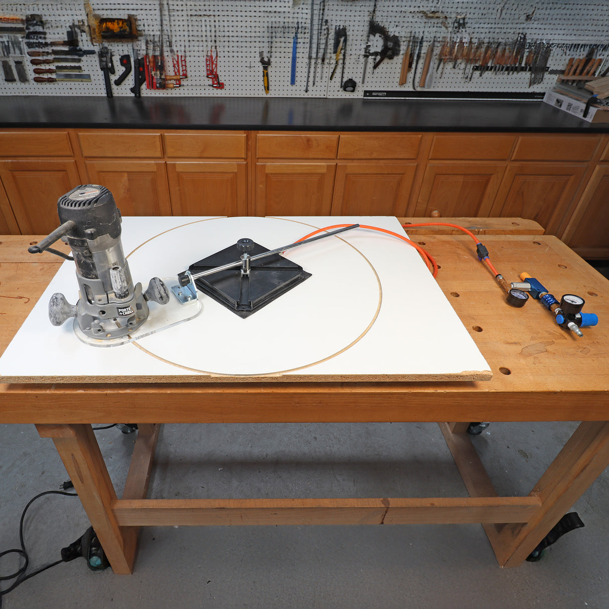 Router circle cutting jig setup on workbench with pneumatic tool and gauges, woodworking shop