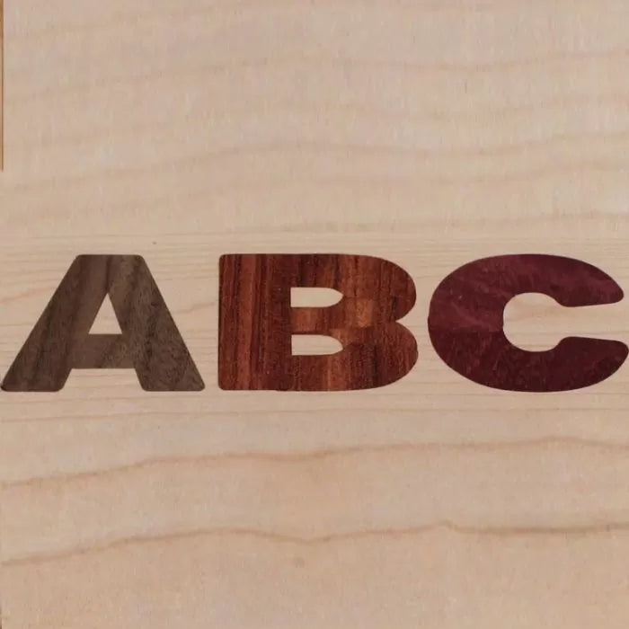 Wood inlay letters A, B, and C on a light wood surface, showcasing woodworking precision.