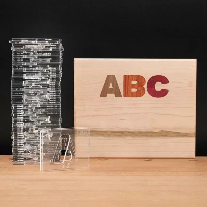 Acrylic router templates stacked beside a wooden box with multicolored ABC inlays for woodworking.