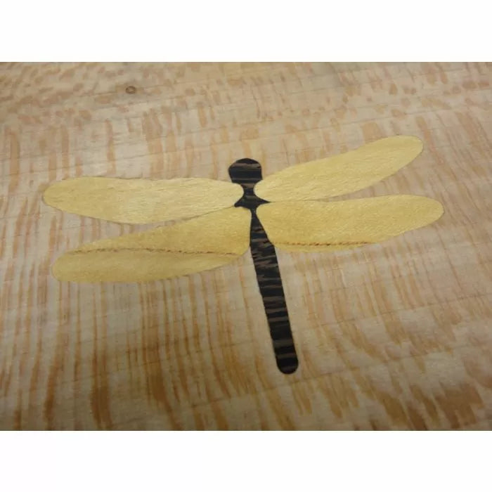 Wood inlay of a dragonfly design on a light wood surface, ideal for woodworking projects.
