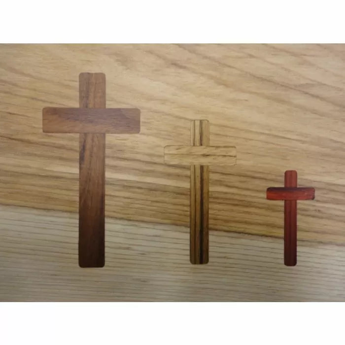 Three wooden cross inlays in different sizes and wood tones on a light wood background