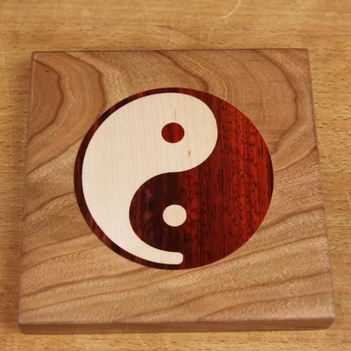 Wood inlay coaster with yin yang symbol on light hardwood background