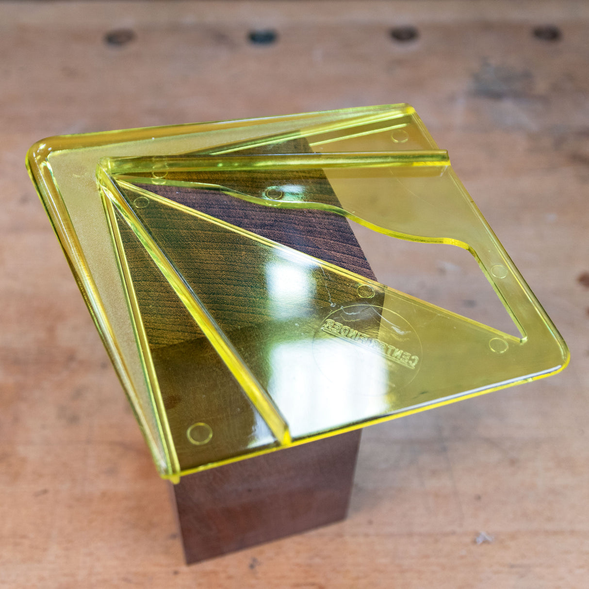 Yellow center finding jig on wood block, used for precise woodworking measurements