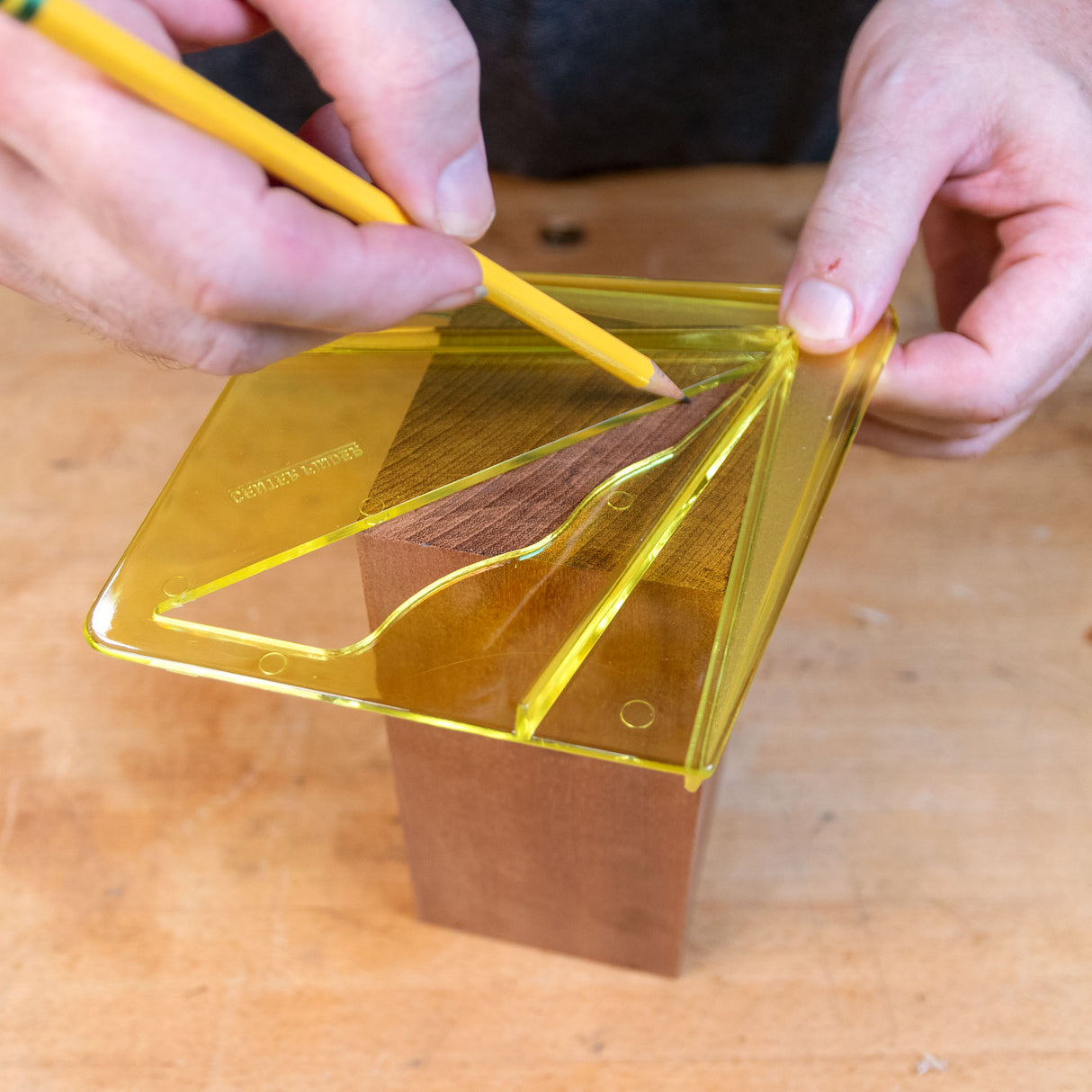 Person using a yellow center finding jig to mark the center of a wooden block.