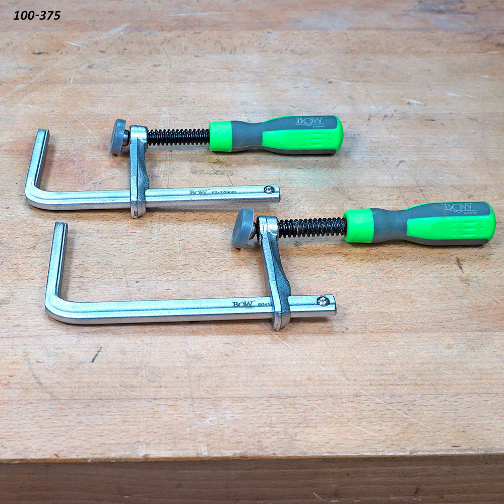 Pair of metal woodworking clamps with green handles on a workbench