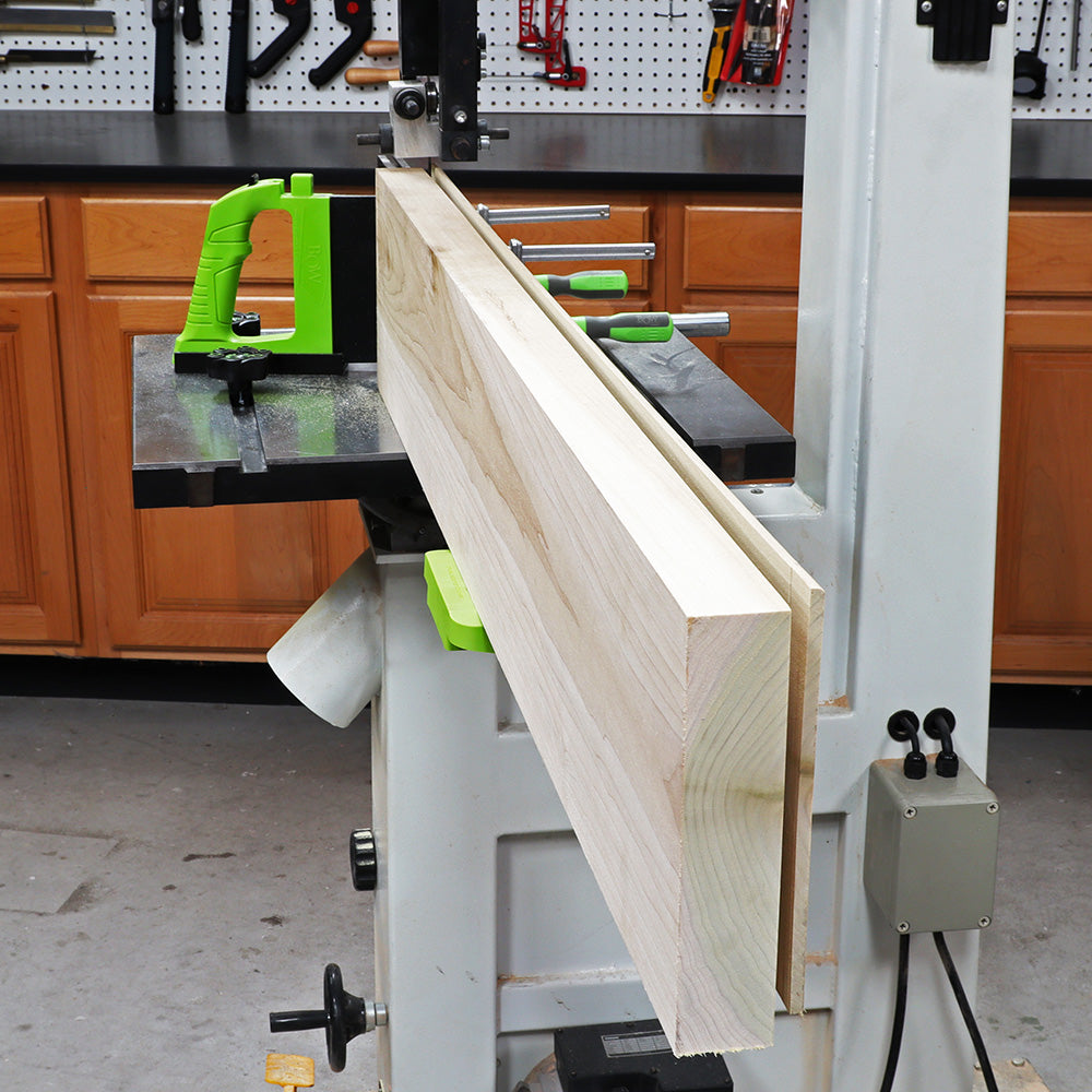 Band saw with resaw guide and push block cutting hardwood board in woodworking shop