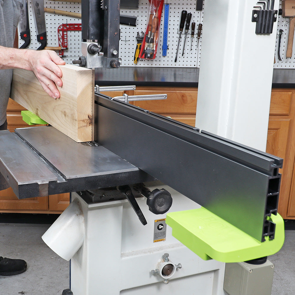 Woodworker guiding thick lumber on a bandsaw with fence system in workshop setting