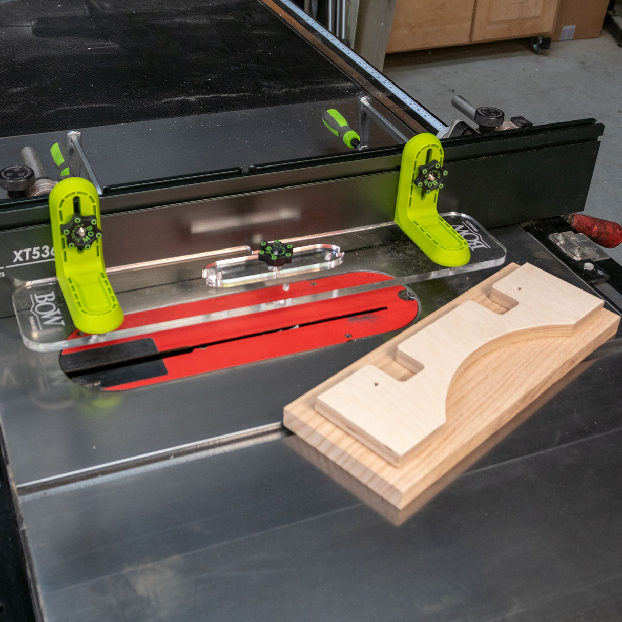 Table saw with L-fence system, safety featherboards, and wooden workpiece in workshop