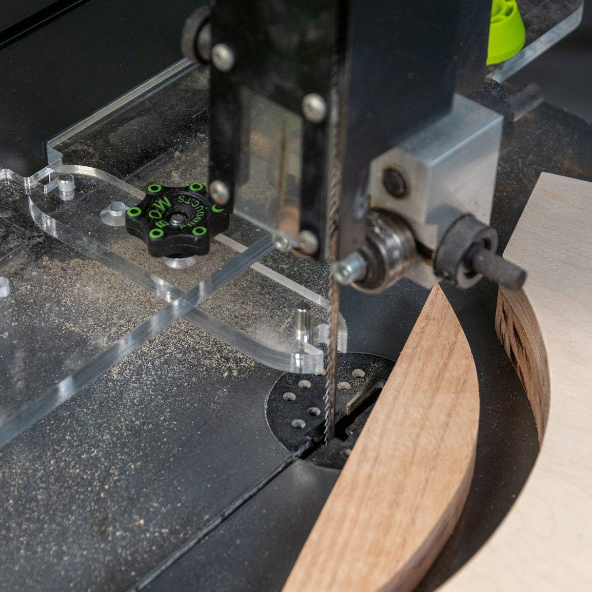 Bandsaw cutting curved wood with clear fence system and dust on table