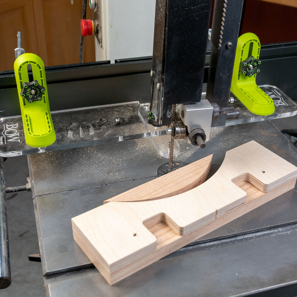 Bandsaw with L-fence system and bright green featherboards cutting wood piece