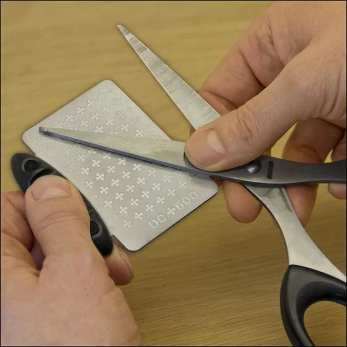 Sharpening scissors blade with a diamond sharpening stone on a wooden surface