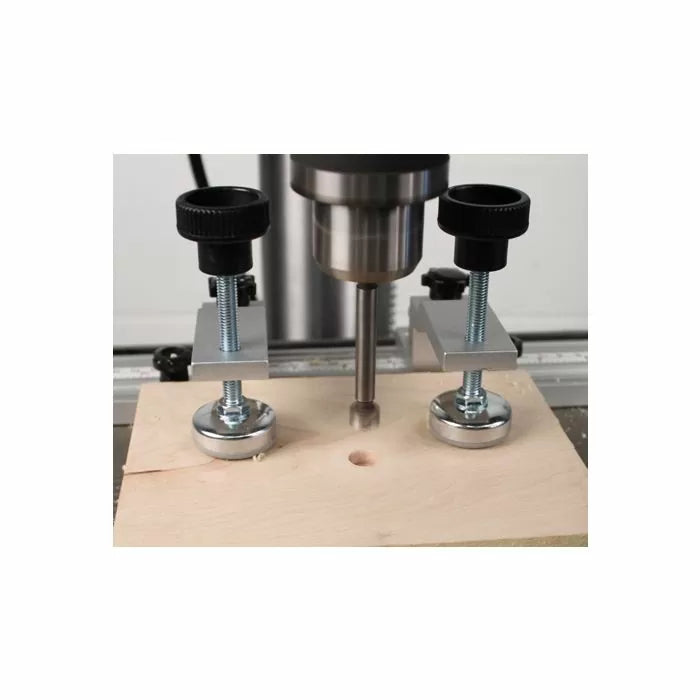 Drill press with woodworking hold-down clamps securing wood for precise drilling