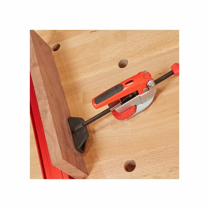 Orange bench clamp securing a wooden board on a workbench for woodworking