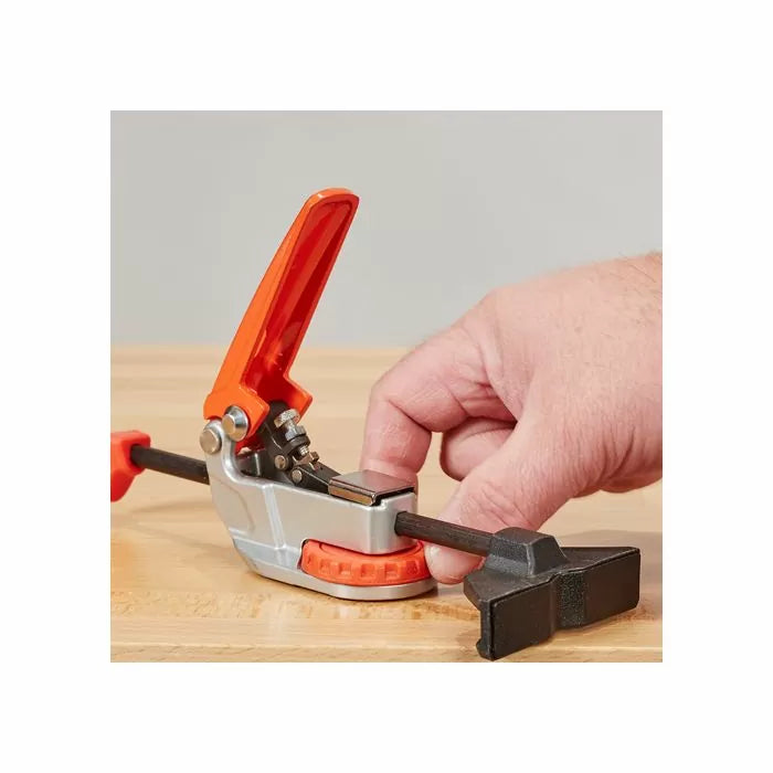 Quick-release woodworking clamp with orange handle on a workbench, hand adjusting clamp.