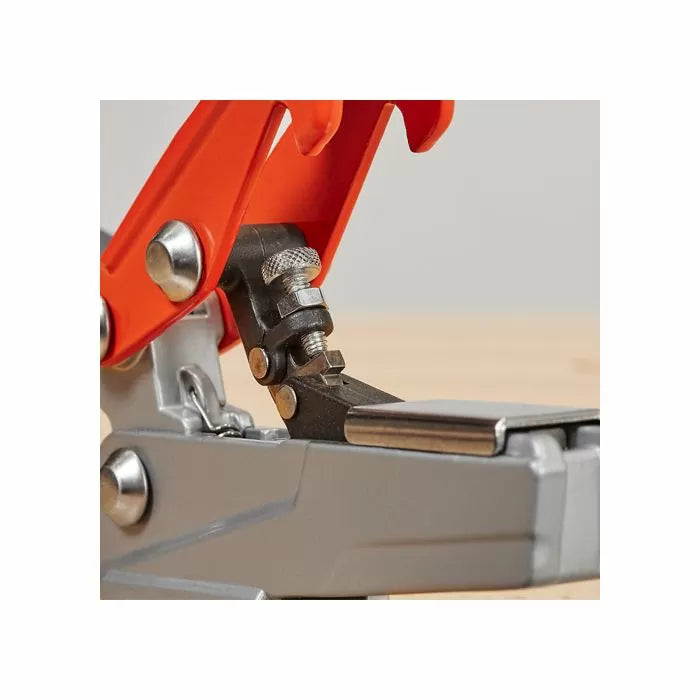 Close-up of a woodworking toggle clamp on a workbench, featuring metal and orange parts.