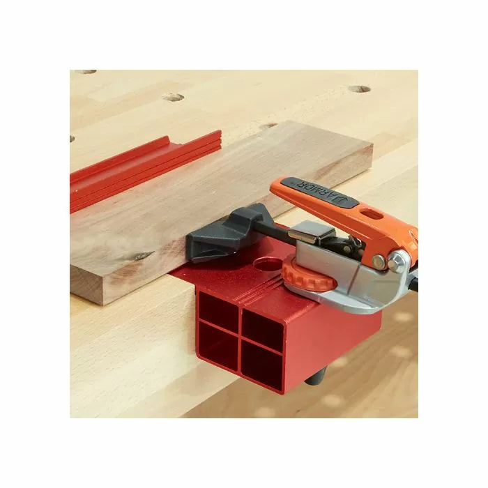 Woodworking bench with red clamping jig and toggle clamp securing a wood board