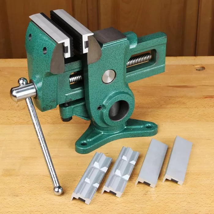Heavy-duty woodworking bench vise with green body and four interchangeable metal jaws on workbench